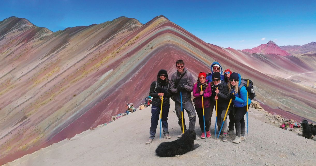 Un viaje en grupo de WeRoad con un perro negro posando en una cresta montañosa, con montañas coloridas y a rayas al fondo.