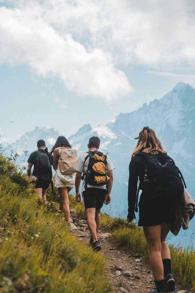 Un gruppo WeRoad visto da dietro, in escursione su uno stretto sentiero di montagna erboso con cime rocciose sullo sfondo.