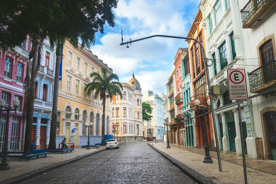 Uno scorcio di una strada acciottolata con binari del tram, fiancheggiata da edifici colorati di epoca coloniale e palme.
