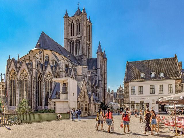 La gente camina por una plaza soleada con una gran catedral gótica y edificios históricos al fondo.