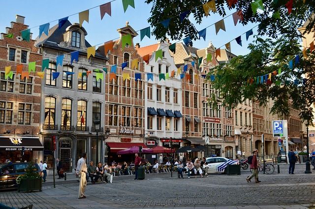 Una soleada plaza adoquinada en una ciudad europea, con gente en los cafés y coloridas guirnaldas de banderas colgando.