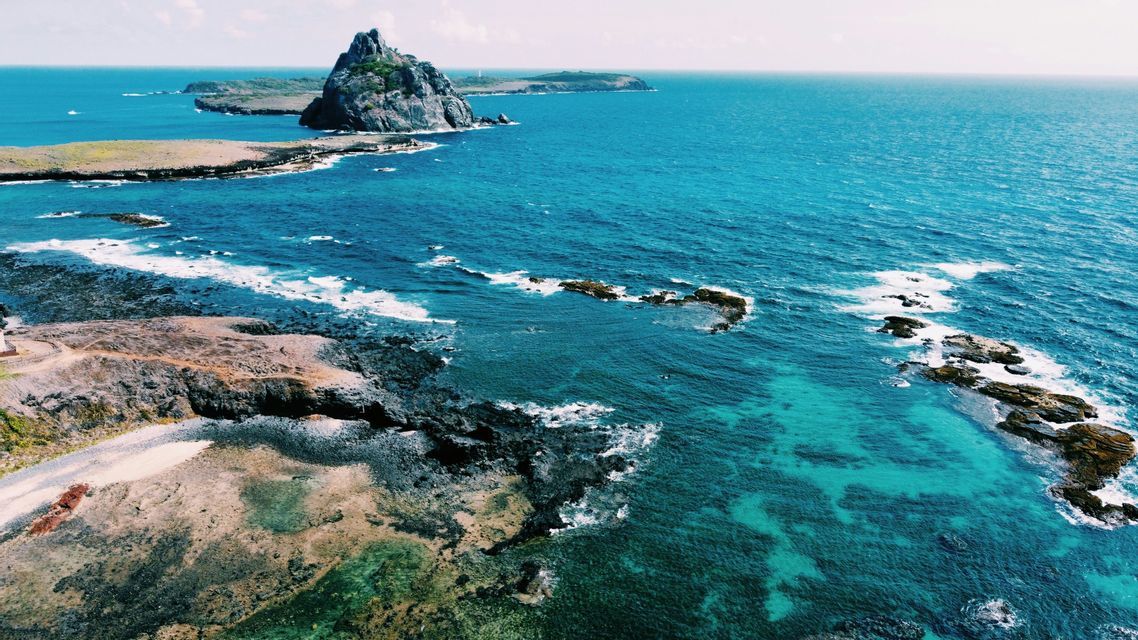 Vista aerea di una costa frastagliata con un'isola rocciosa che si staglia in un vivace oceano turchese.