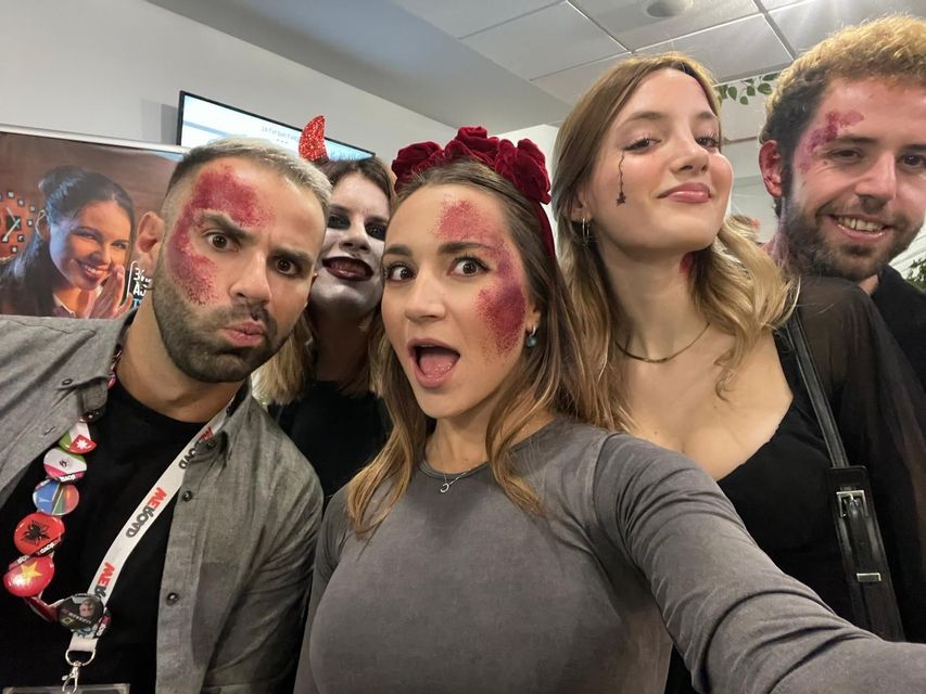 Un gruppo di persone con trucco in stile Halloween e glitter rosso posa insieme per un selfie, facendo facce giocose.