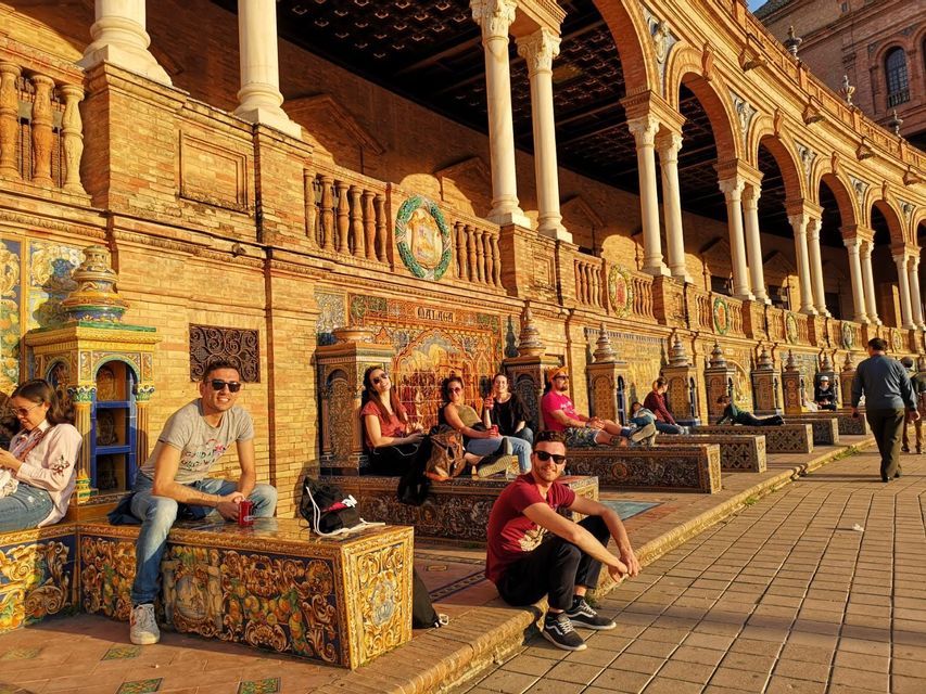 Un gruppo WeRoad in relax su panchine decorate e piastrellate di fronte a un edificio ad arco, all'ora d'oro.