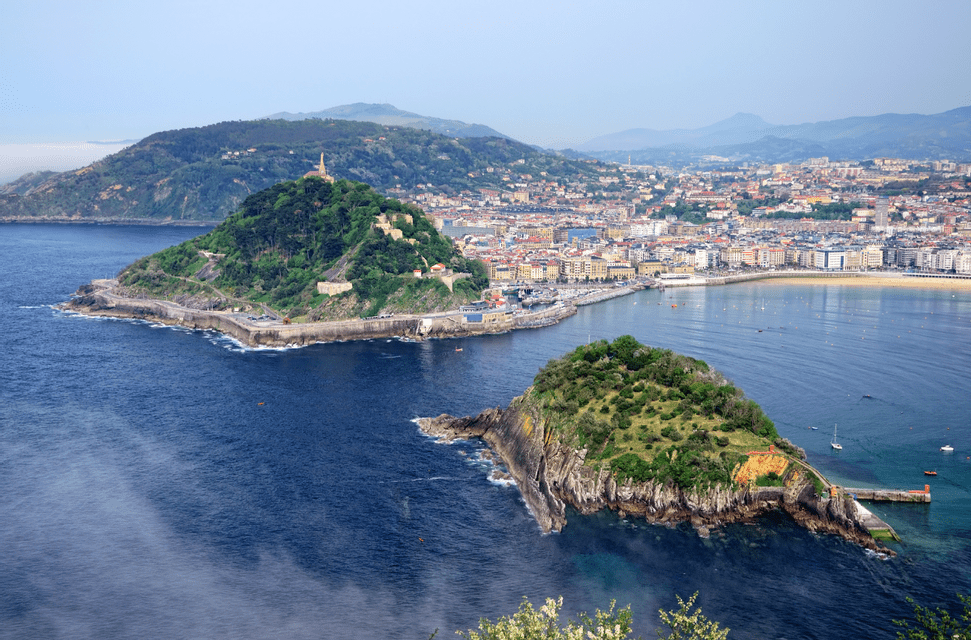 Una vista aerea di due isole verdi e lussureggianti in una baia blu profonda, con una città costiera e dolci colline sullo sfondo.