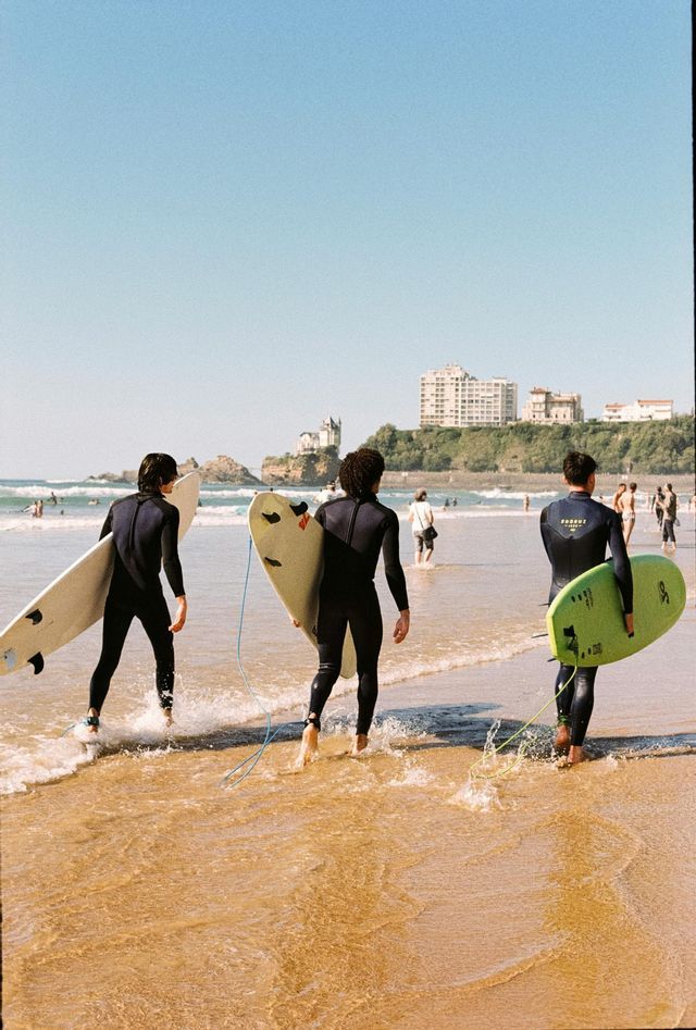 Un viaggio di gruppo WeRoad: tre surfisti in muta che trasportano le tavole da surf mentre entrano in mare dalla spiaggia.