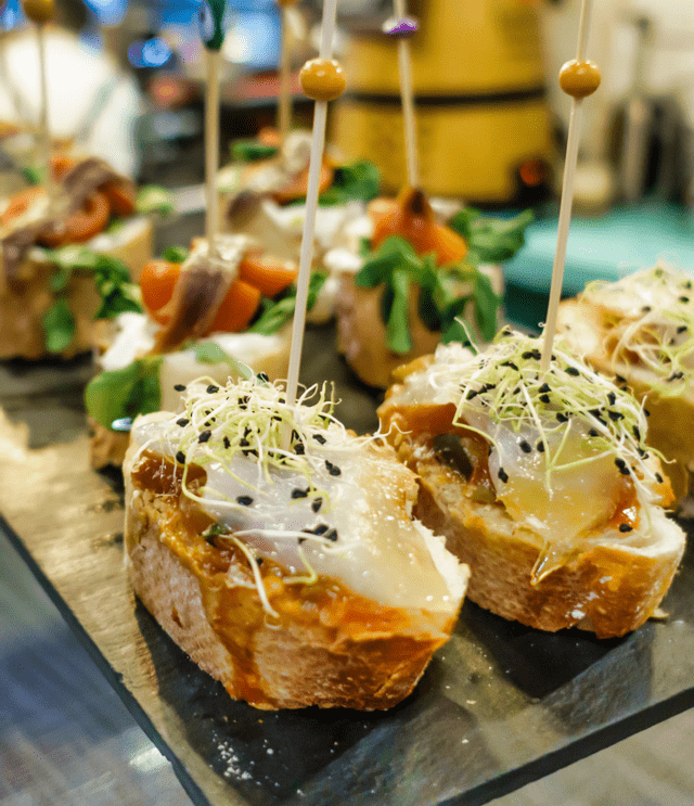Un primo piano di vari pintxos spagnoli con pesce e germogli su un piatto da portata scuro, ognuno fissato con uno stuzzicadenti.