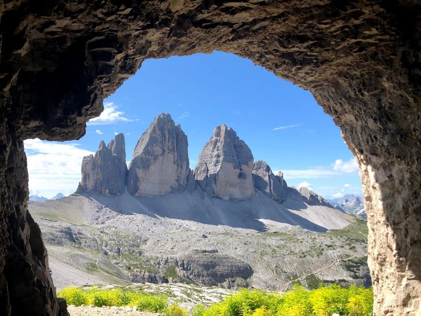 Una vista de una cordillera escarpada con laderas rocosas, enmarcada por la entrada de una cueva oscura bajo un cielo azul claro.