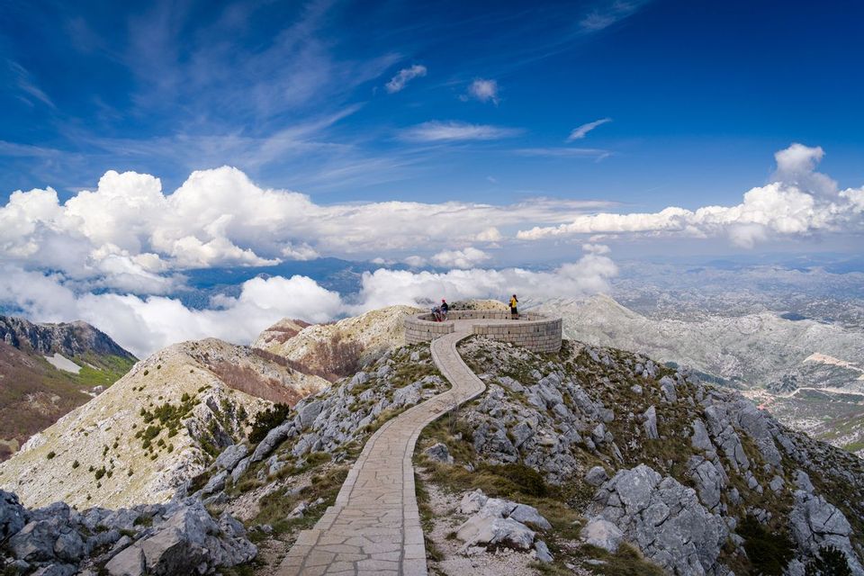 Un sentiero in pietra tortuoso porta a un belvedere circolare su una vetta di montagna, dove un gruppo WeRoad si gode la vista panoramica.