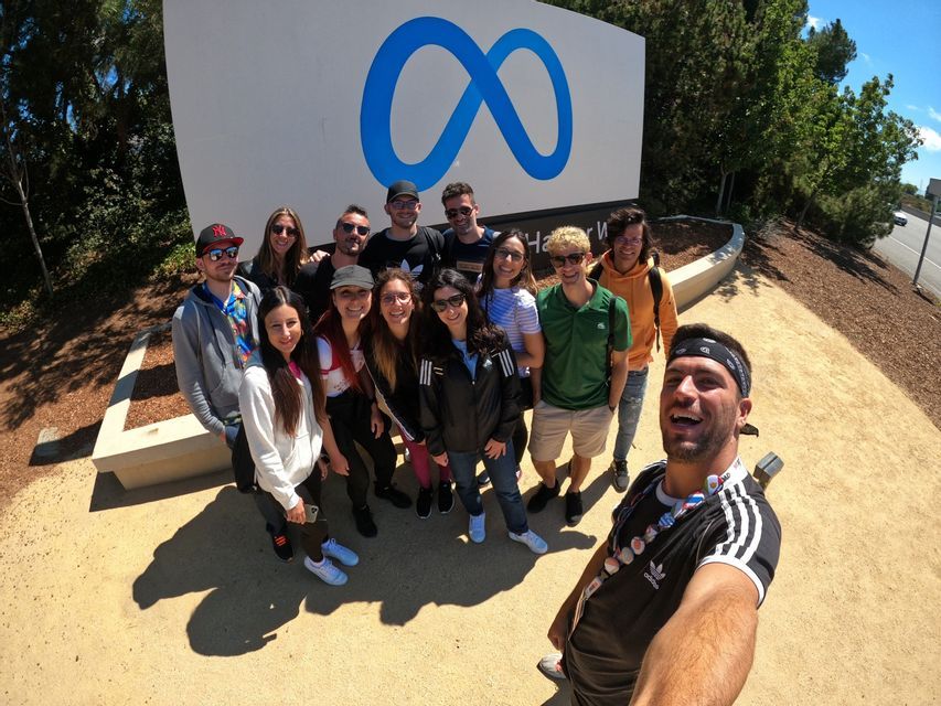 Un gruppo WeRoad si fa un selfie, sorridendo insieme davanti al grande cartello esterno con il logo Meta in una giornata di sole.