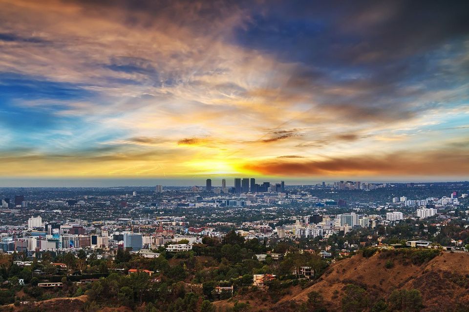 Un panorama urbain étendu vu d'une colline, avec des gratte-ciel à l'horizon sous un ciel de coucher de soleil spectaculaire et coloré.