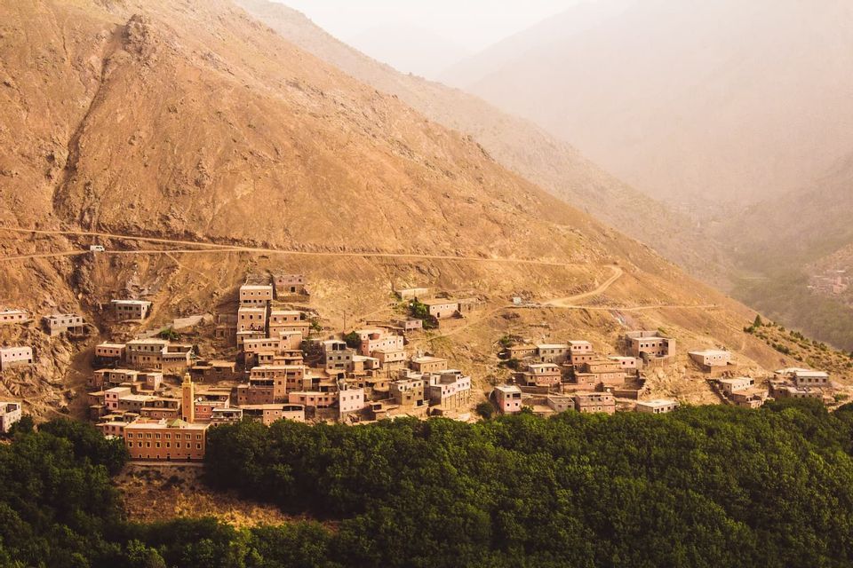 Un village aux bâtiments ocre-rouge, dont une mosquée, accroché à un flanc de montagne escarpé au-dessus d'une dense forêt verte.