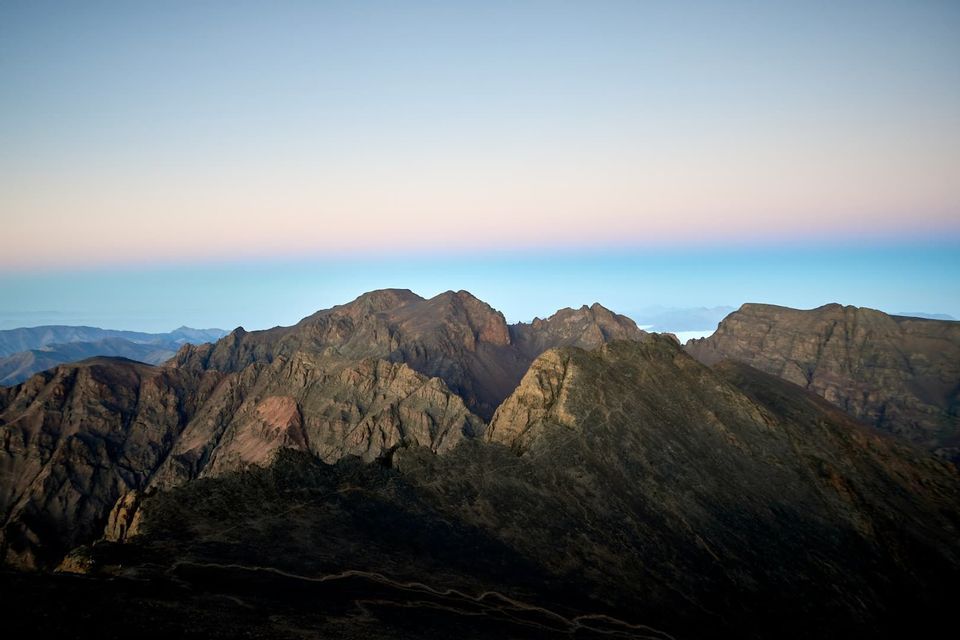Las cumbres irregulares de una oscura cordillera se ven contra un cielo despejado con un gradiente rosa y azul al amanecer.
