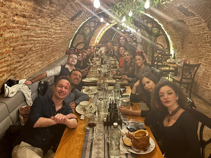 Un gruppo WeRoad in maschere di Halloween è seduto a un lungo tavolo da pranzo in un ristorante con soffitti a volta in mattoni, sorridendo per una foto.