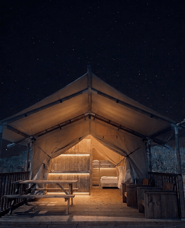 Una grande tenda glamping illuminata con un ponte in legno e un tavolo da picnic sotto un cielo stellato.
