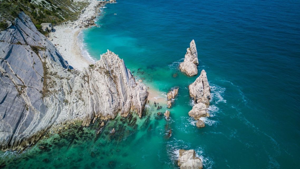 Una vista aerea di alte formazioni rocciose bianche e scogliere lungo una costa con acqua turchese e blu intenso.