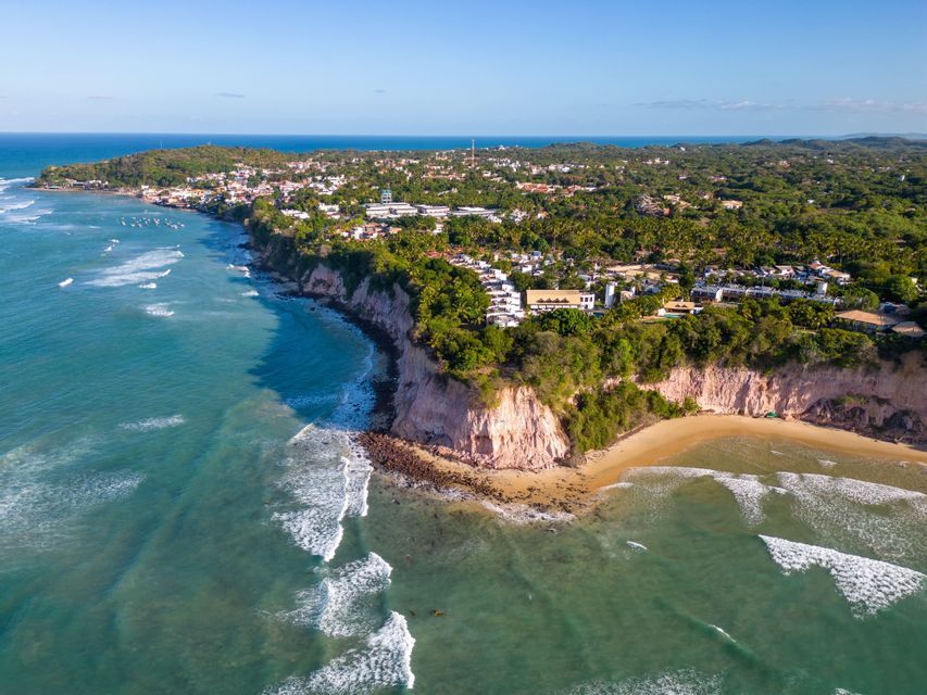 Una vista aérea de un pueblo costero construido sobre acantilados exuberantes con vistas a una playa de arena y al océano.
