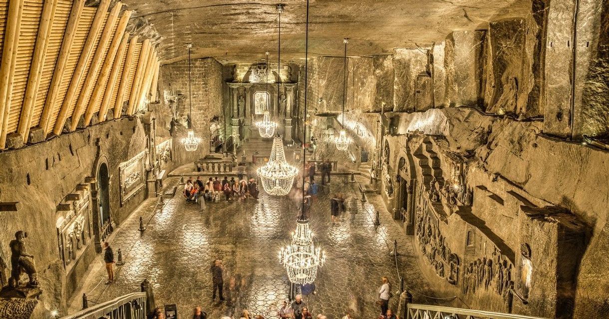 Una vista dall'alto di un'ampia cavità sotterranea scavata nella roccia, con sfarzosi lampadari che illuminano i turisti su un pavimento riflettente.