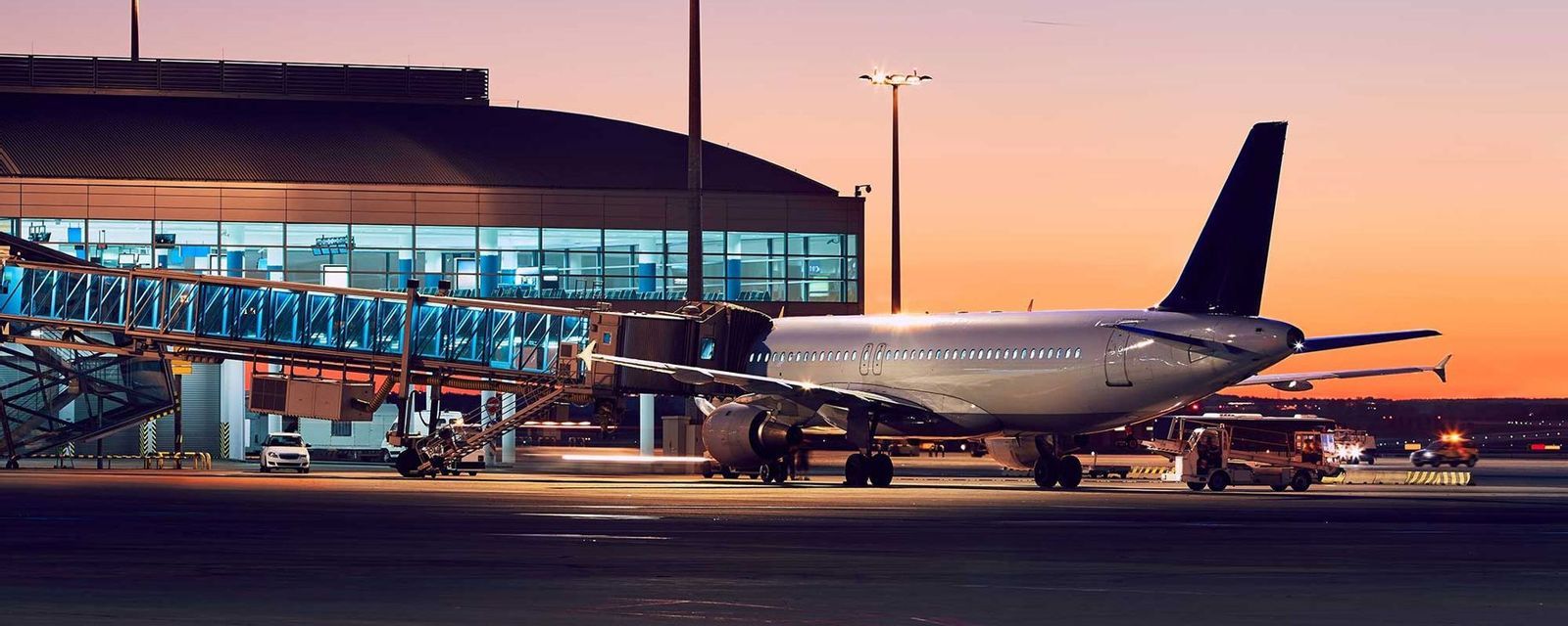 Un aereo è parcheggiato al gate di un terminal aeroportuale, collegato da un finger durante un tramonto colorato.