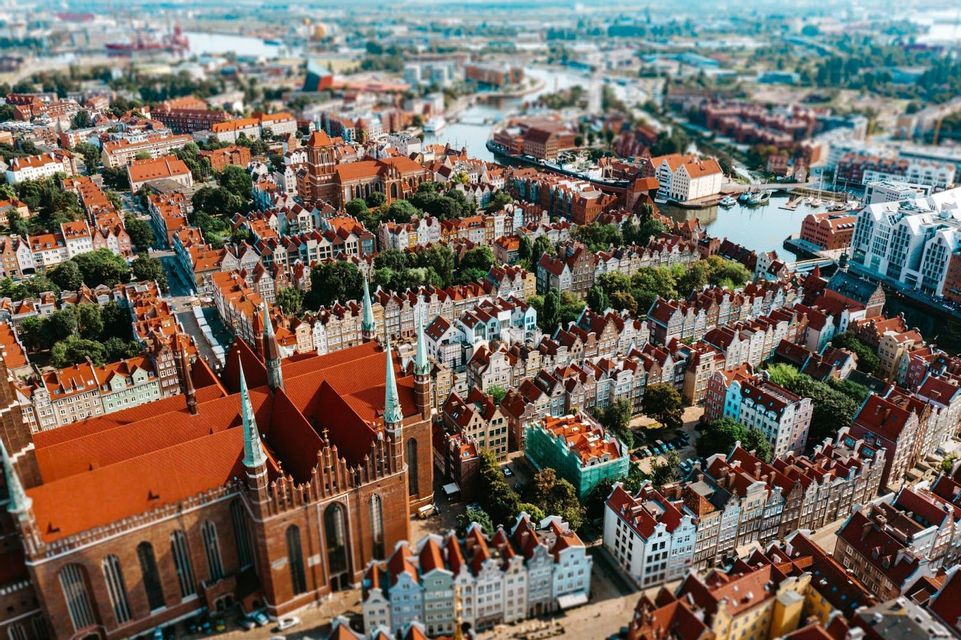 Una veduta aerea in tilt-shift di una città storica con tetti in tegole rosse, una grande cattedrale e un fiume che serpeggia al suo interno.