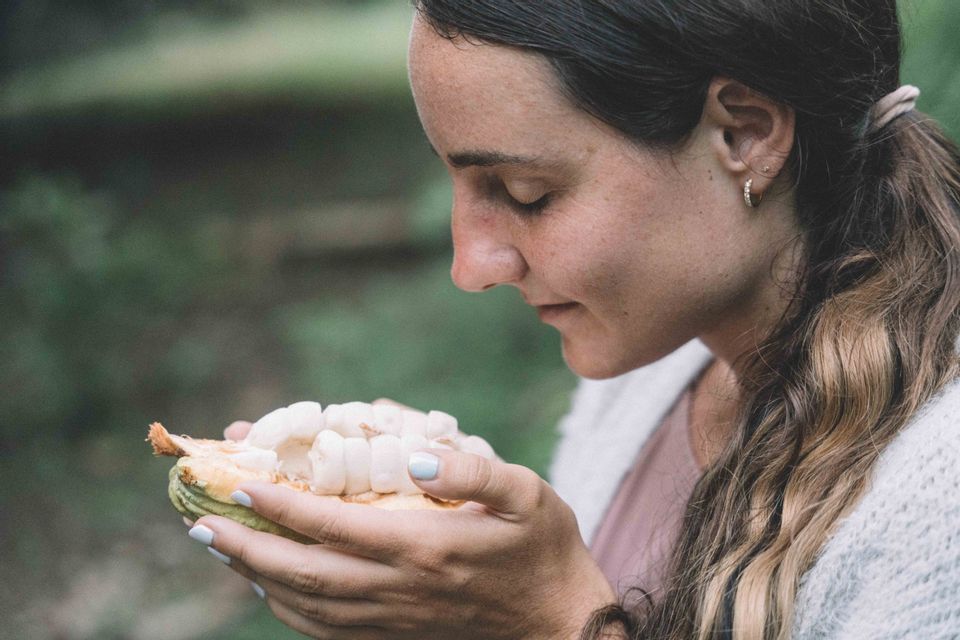 Una donna di profilo, con gli occhi chiusi, che annusa la polpa bianca di un baccello di cacao appena aperto.