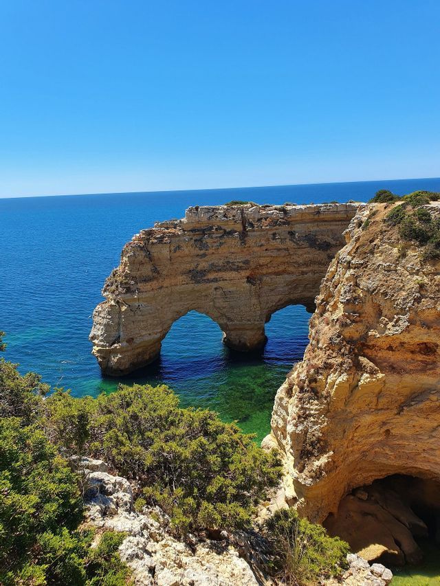 Una grande formazione rocciosa costiera presenta due archi naturali su acque turchesi in una giornata di sole.
