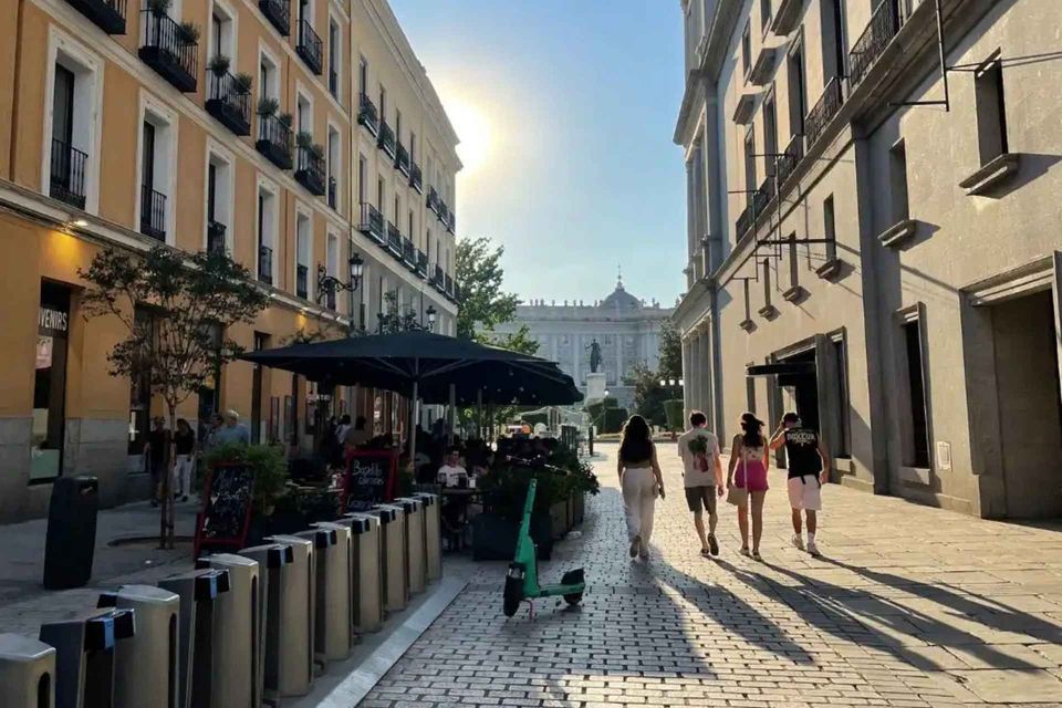 Quattro persone di un gruppo WeRoad camminano lungo una soleggiata strada acciottolata fiancheggiata da edifici, con un palazzo visibile in lontananza.