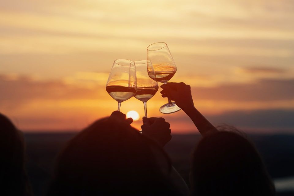 Sagome di un gruppo WeRoad che brinda con tre calici di vino bianco al tramonto arancione.