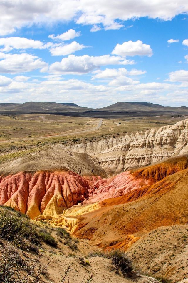 Un canyon con formazioni rocciose rosse, arancioni e gialle in un paesaggio arido sotto un cielo parzialmente nuvoloso.