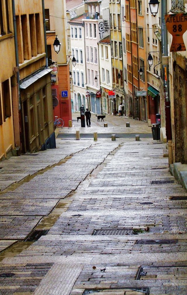 Una ripida e bagnata strada acciottolata scende attraverso uno stretto vicolo fiancheggiato da alti e colorati edifici storici.