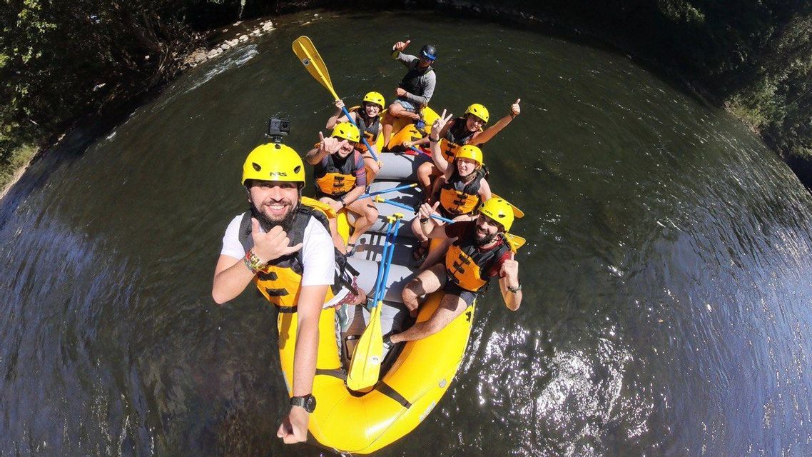 Un gruppo WeRoad si scatta un selfie dall'alto mentre fa rafting su un fiume con un gommone giallo, tutti sorridenti e con i caschi.