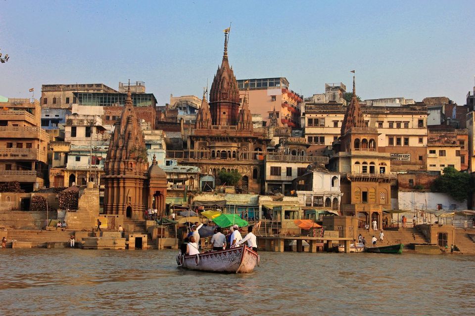 Un viaje en grupo de WeRoad en barco por un río, pasando por una ciudad concurrida con templos tradicionales y escalones de piedra en la orilla.