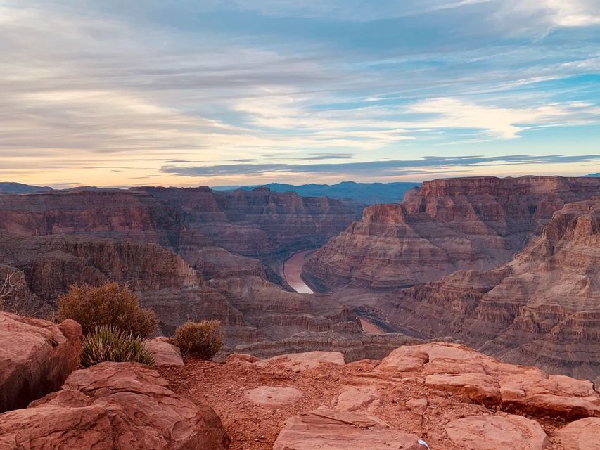 Vue panoramique sur un canyon profond avec une rivière sinueuse, depuis un promontoire rocheux sous un ciel nuageux au coucher du soleil.