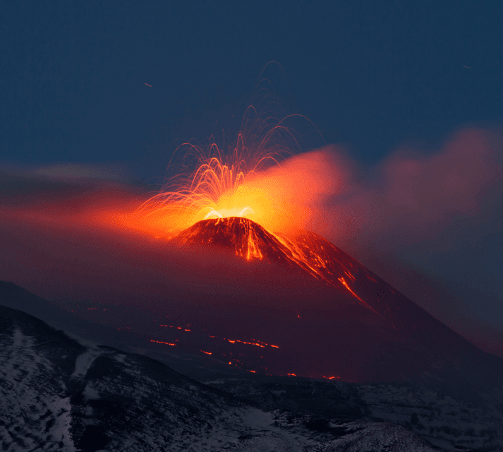 Un vulcano erutta di notte, vomitando lava incandescente e scintille dal suo cratere nel cielo scuro, mentre è circondato dal fumo.