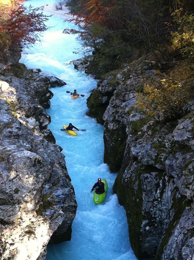 Eine WeRoad-Gruppe paddelt auf einem leuchtend blauen Fluss, der sich aus der Vogelperspektive durch eine enge, felsige Schlucht schlängelt.