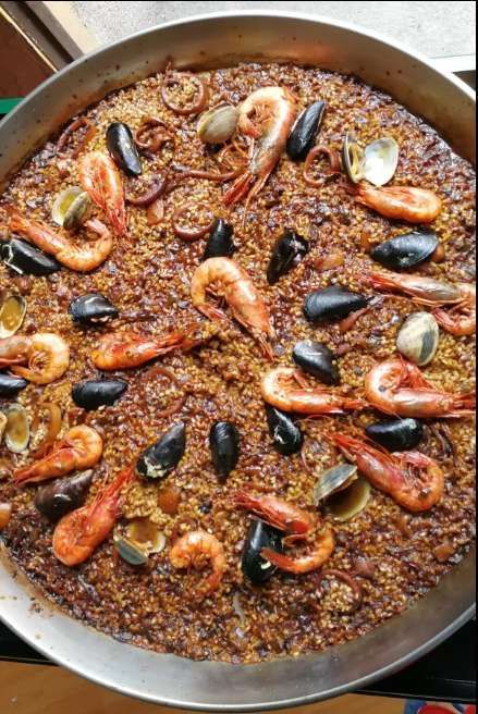 Una paella tradizionale di mare con gamberi, cozze e vongole servita in una grande padella di metallo.