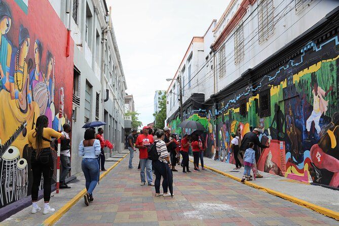 Un grupo de personas se encuentra en una calle estrecha y pavimentada, observando murales coloridos que cubren los lados de los edificios.