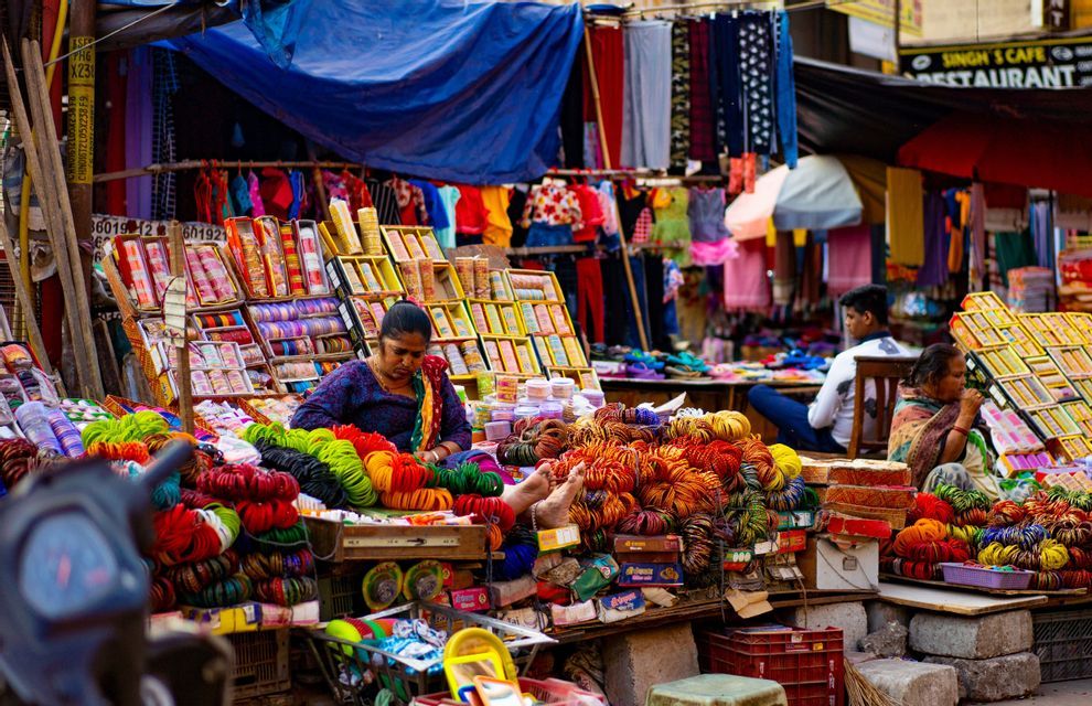 Una donna vende braccialetti e bracciali colorati dalla sua bancarella in un affollato mercato di strada all'aperto.
