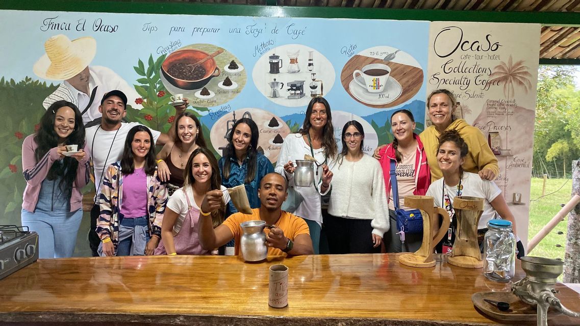 Un viaggio di gruppo WeRoad sorride per una foto durante una degustazione di caffè, in posa dietro un bancone di legno con un murale sullo sfondo.