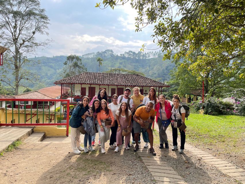 Un viaje en grupo de WeRoad posa para una foto en un sendero frente a un edificio rural, con exuberantes colinas verdes de fondo.