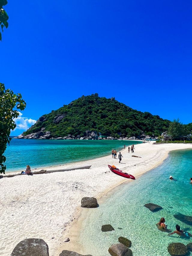 Un groupe WeRoad avance sur un étroit banc de sable blanc menant à une île luxuriante baignée d'eau turquoise cristalline.
