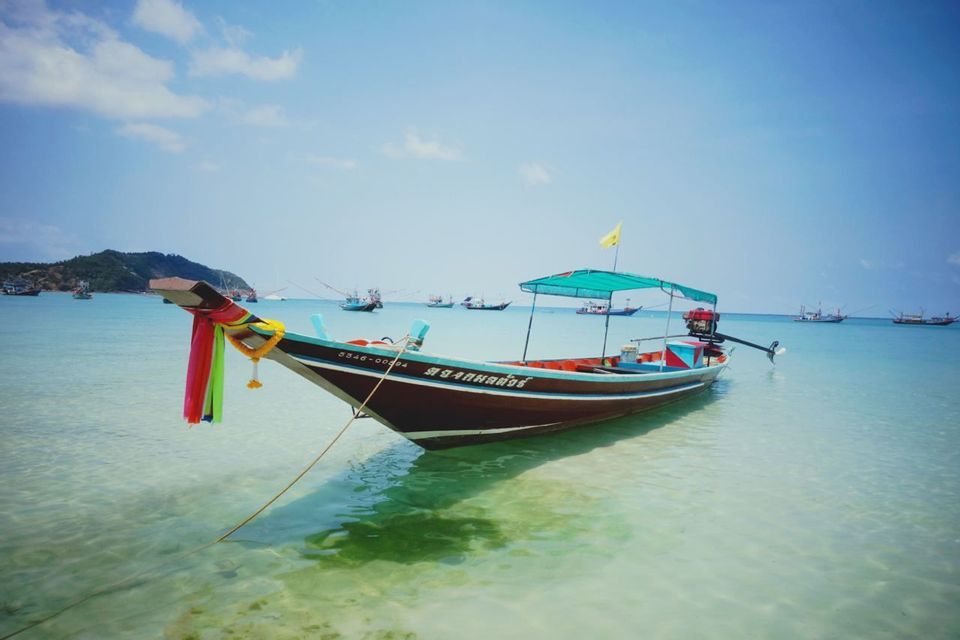 Un bote tradicional de cola larga, decorado con cintas, flota en aguas tranquilas de color turquesa con una isla verde en el horizonte.
