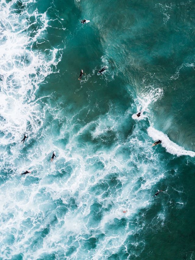 Vista aerea dall'alto di surfisti che galleggiano sulle tavole in acque turchesi tra onde bianche e spumeggianti.