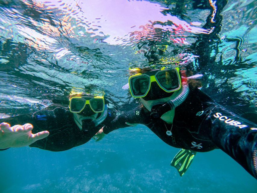 Due persone in viaggio di gruppo WeRoad si scattano un selfie subacqueo con maschere da snorkeling in acqua cristallina.