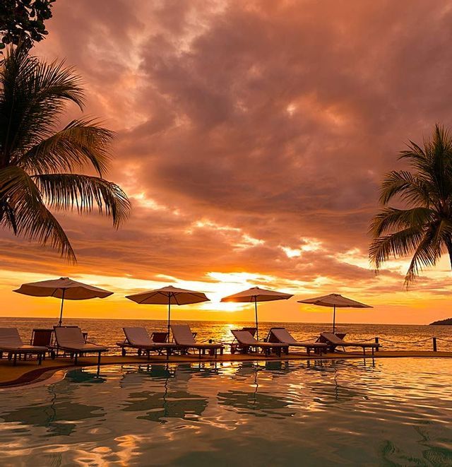 Sdraio e ombrelloni su una terrazza a bordo piscina, con vista sull'oceano durante un tramonto arancione.