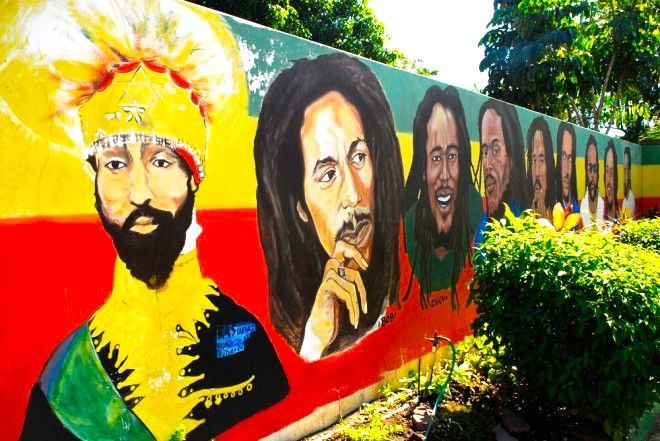 Ein farbenfrohes Wandgemälde im Freien zeigt ein großes Porträt von Haile Selassie I. neben mehreren Porträts des Musikers Bob Marley.