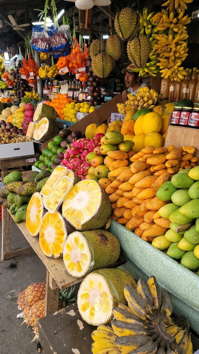 Ein Obstmarktstand ist vollgepackt mit einer Vielzahl tropischer Früchte, darunter geschnittene Jackfrucht, Mangos, Drachenfrucht und Durian.