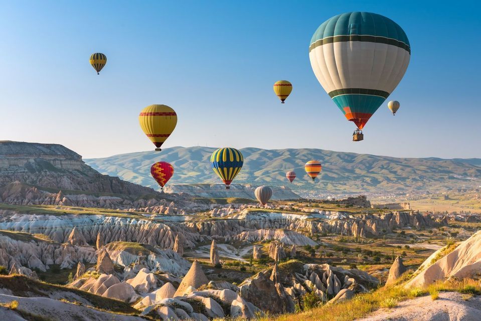 Des montgolfières colorées flottant au-dessus d'un vaste paysage de formations rocheuses coniques uniques sous un ciel bleu clair.