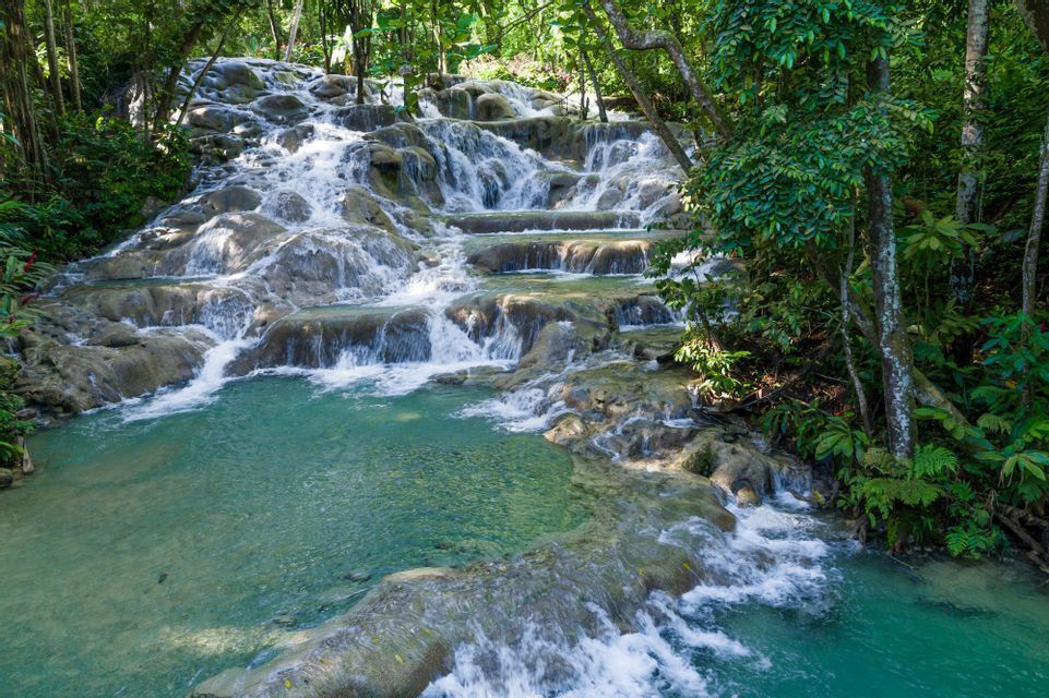 Ein terrassierter Wasserfall stürzt über Felsen in ein klares, türkisfarbenes Becken, umgeben von üppiger grüner Dschungelvegetation.
