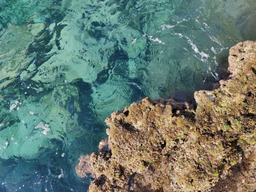 Una vista dall'alto di acqua cristallina turchese che lambisce una formazione rocciosa scabra e coperta di muschio.